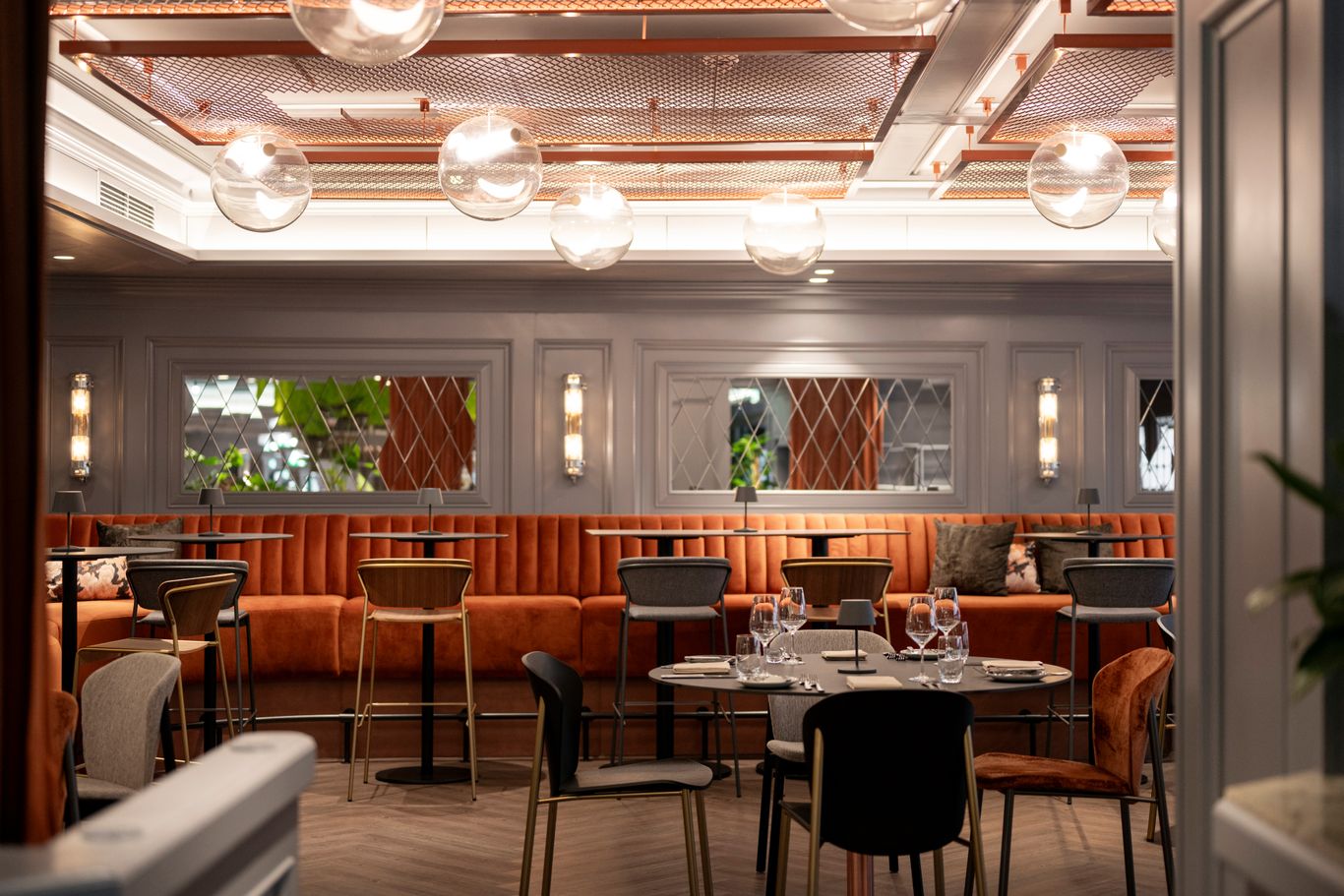 A modern hotel restaurant interior with warm lighting, orange booth seating, and tables set for dining.